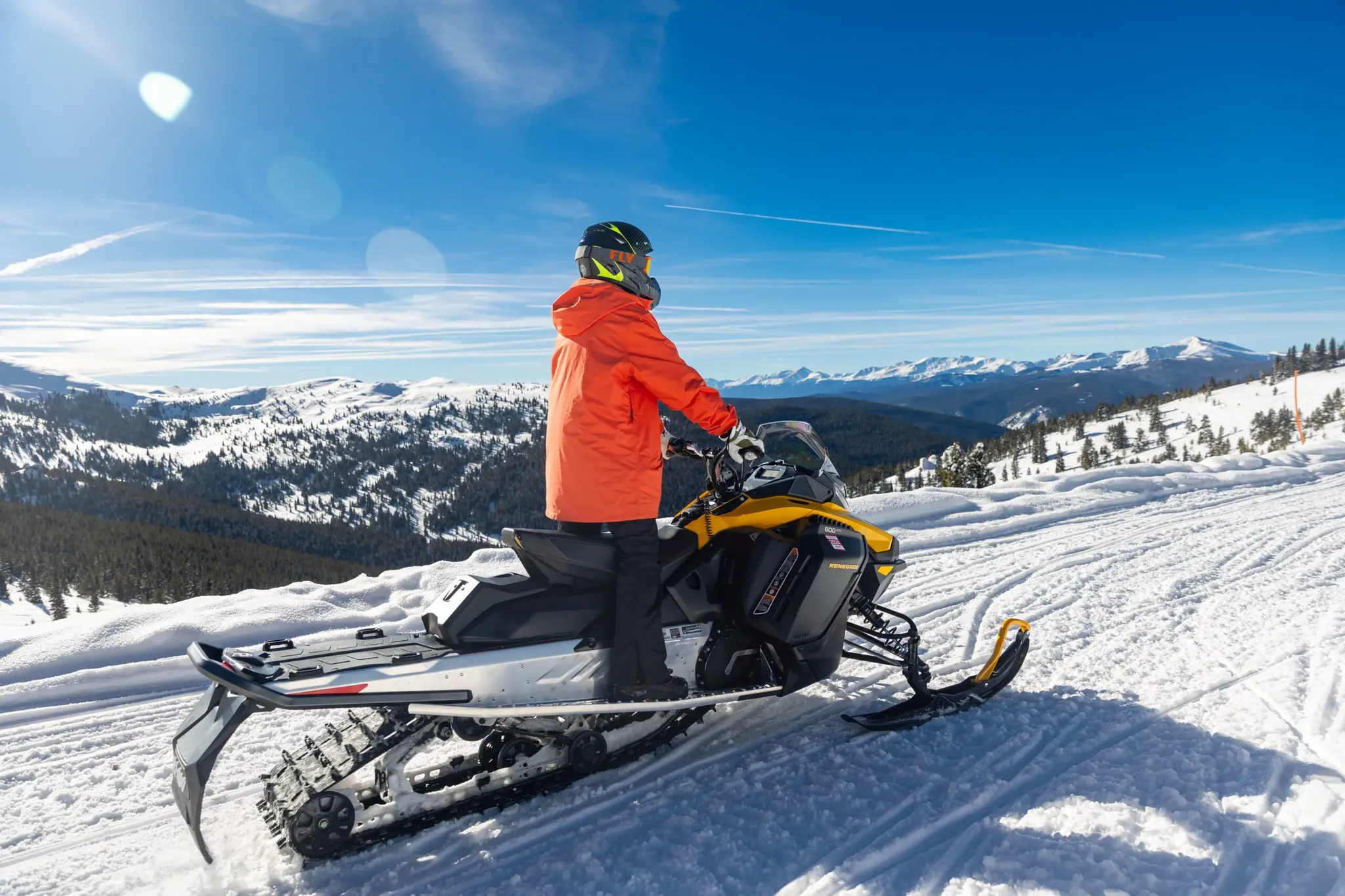 single snowmobile rider on snowy trail with sweeping mountain views.